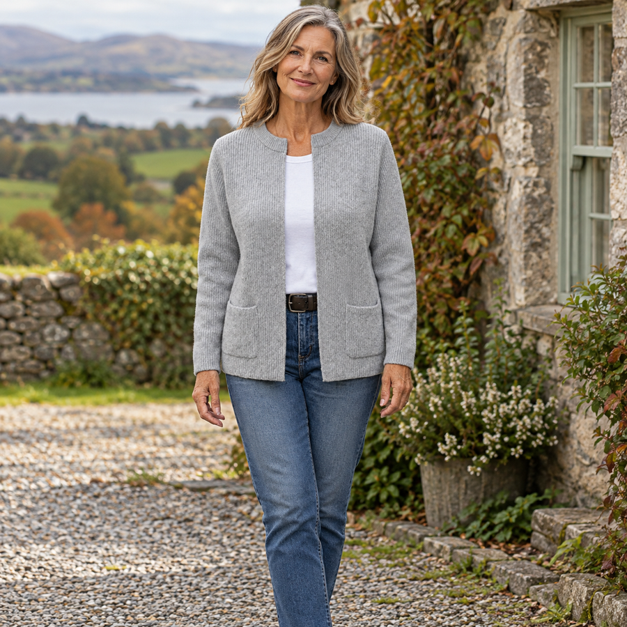 AI-generated lifestyle image of a mature woman wearing the grey Kerry Zip-Up Knit Cardigan beside an Irish stone cottage